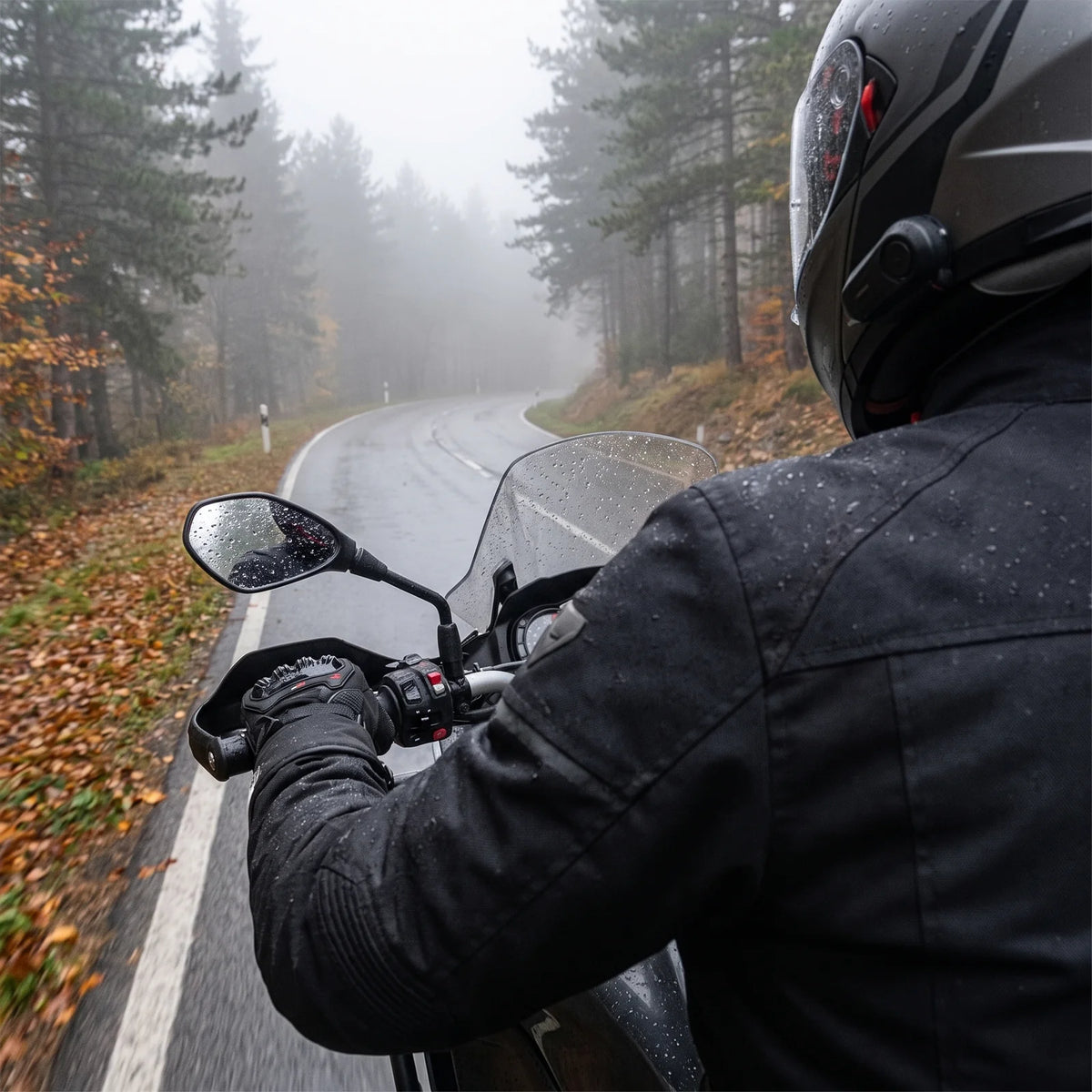 Motorcyclist with winter gloves on the handlebar on a wet mountain road in fog